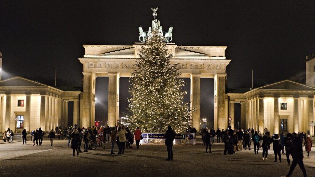 The Brandenburg Gate in Berlin lit at night with a tall decorated Christmas tree in front of it